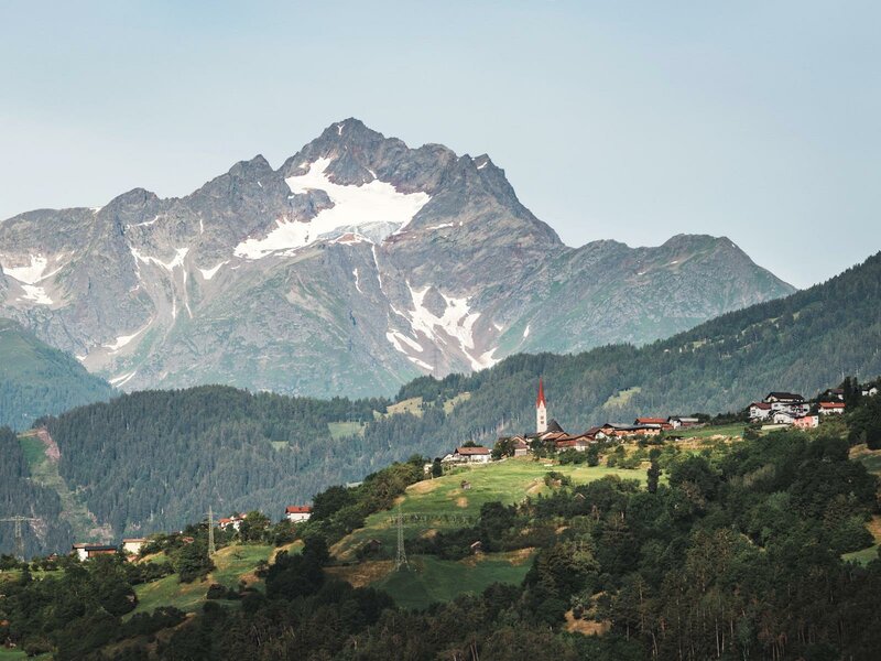 Ein Bergdorf mit Kirchturm vor alpiner Bergkulisse
